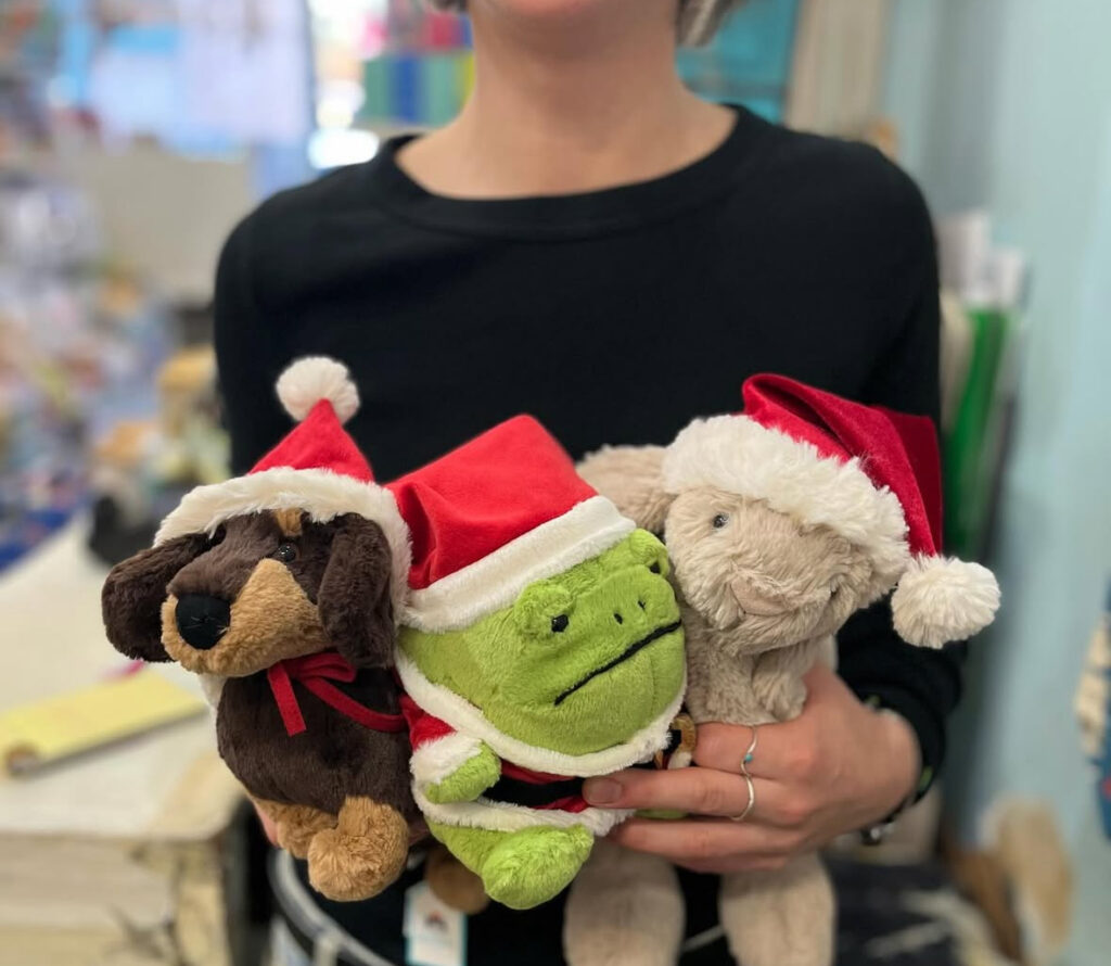 Person in dark colored top holding 3 stuffed animals wearing Santa Claus hats